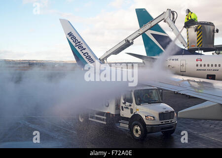 Die Bodenbesatzung des Flughafens sprüht Enteisflüssigkeit auf den Flugzeugflügel der Boeing 737, um Eis und Schnee vor dem Start im Winter zu entfernen Stockfoto