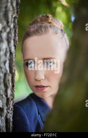 Junge Frau spähte durch Baumstämme Stockfoto