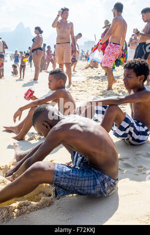 RIO DE JANEIRO, Brasilien - 8. Februar 2015: Junge Brasilianer sitzen am Strand von Ipanema Strand an einem überfüllten Sommernachmittag. Stockfoto