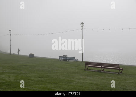 Frau, die mit einem Hund im Nebel auf einer Strandpromenade läuft, Großbritannien Stockfoto