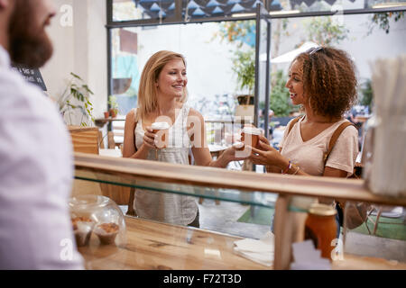 Aufnahme von zwei jungen Freundinnen lächelnd, als sie ihre Kaffee-Bestellung von der Café-Theke abholen. Stockfoto