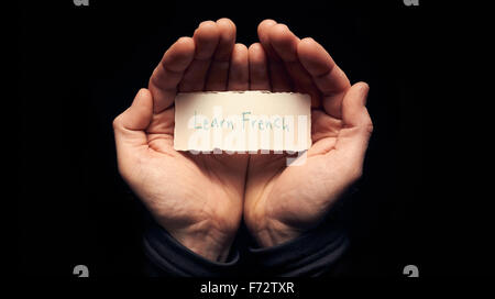Ein Mann hält eine Karte in der hohlen Hand mit eine handschriftliche Nachricht drauf, Französisch lernen. Stockfoto