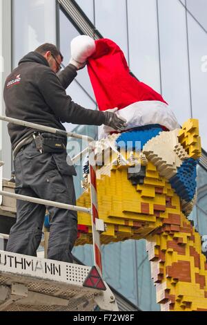 Berlin, Deutschland. 24. November 2015. Ein Arbeiter legt eine rote Weihnachtsmütze auf eine Giraffe aus Legosteinen vor Legoland am Potsdamer Platz in Berlin, Deutschland, 24. November 2015 gebaut. Foto: PAUL ZINKEN/DPA/Alamy Live-Nachrichten Stockfoto