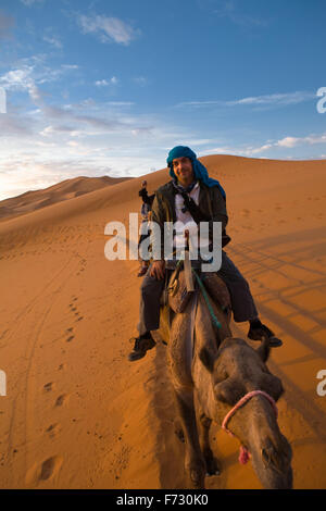 Ein Tourist der Kamelritt und bewundern Sie den Sonnenuntergang von einem Hügel aus. Einige Schleifen Hügel am Erg Chebbi in der Wüste Sahara.  Ers sind groß Stockfoto