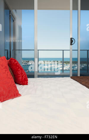 Bild einer Zeitschrift auf einem Bett mit roten Sitzkissen, in einem Raum mit einem Fenster mit Blick auf das Meer Stockfoto