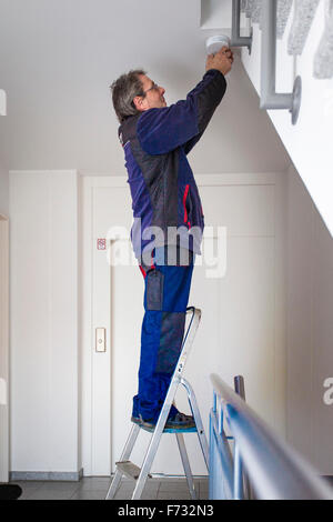 Hausmeister in einem Treppenhaus montiert und überprüft einen Rauchmelder Stockfoto