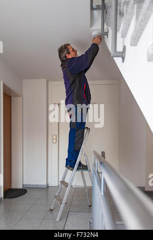 Hausmeister in einem Treppenhaus montiert und überprüft einen Rauchmelder Stockfoto