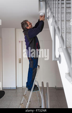 Hausmeister in einem Treppenhaus montiert und überprüft einen Rauchmelder Stockfoto