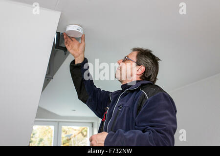 Hausmeister in einem Treppenhaus montiert und überprüft einen Rauchmelder Stockfoto