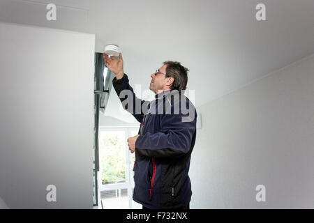 Hausmeister in einem Treppenhaus montiert und überprüft einen Rauchmelder Stockfoto