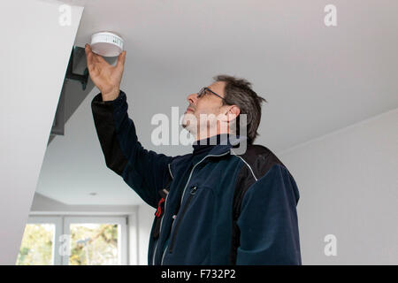 Hausmeister in einem Treppenhaus montiert und überprüft einen Rauchmelder Stockfoto