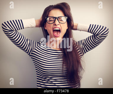 Wütende junge Geschäftsfrau in Gläser stark mit offenem Mund wild schreiend und Kopf die Hände haltend. Getönten Closeup portrait Stockfoto