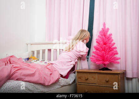 Ein Mädchen spähte durch die Vorhänge in ihrem Schlafzimmer in der Nacht zu Weihnachten. Stockfoto