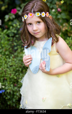 Junges Mädchen mit Blumen im Haar auf einer Gartenparty, hält einen Papier-Schmetterling. Stockfoto