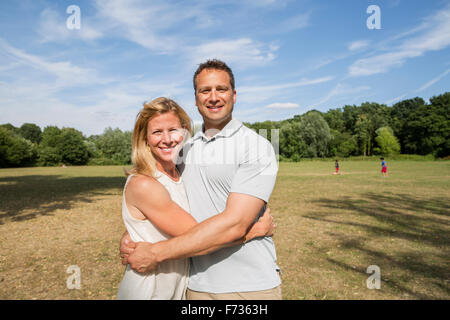 Paar steht in einem Park, lächelnd und umarmen. Stockfoto
