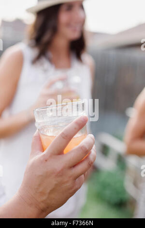 Nahaufnahme von einer Hand hält einen Drink, eine Frau im Hintergrund. Stockfoto