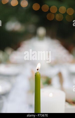 Eine brennende Kerze auf einem Tisch set mit Teller und Gläser, Essen und trinken in einem Garten. Stockfoto