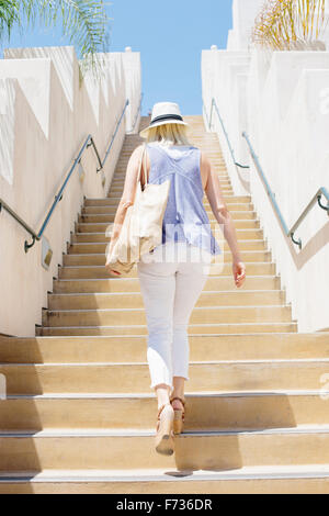 Blonde Frau trägt einen Hut, eine Treppe hinaufzugehen. Stockfoto