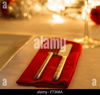 Tabelle festgelegt für das Weihnachtsessen, mit Kugeln und Lametta und Lichterketten dekoriert. Messer, Gabel und rot Serviette. Stockfoto