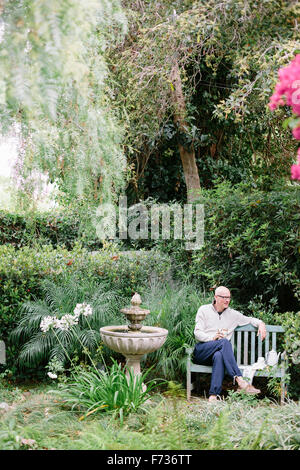 Mann sitzt auf einer Holzbank in einem Garten eine Pause. Stockfoto