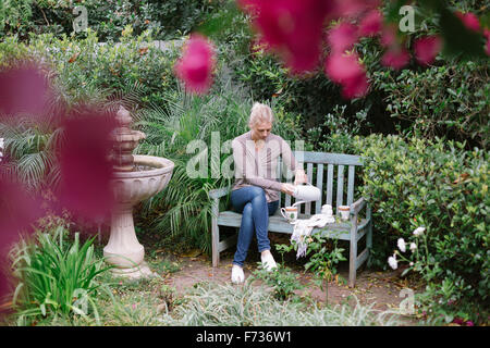 Frau sitzt auf einer Holzbank in einem Garten eine Pause. Stockfoto
