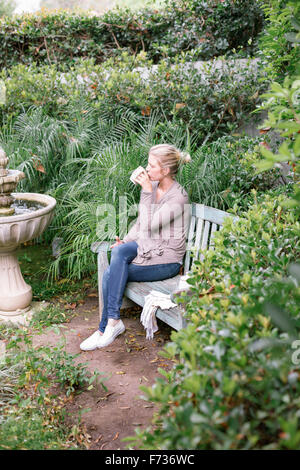 Frau sitzt auf einer Holzbank in einem Garten eine Pause. Stockfoto