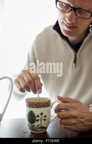 Mann sitzt an einem Tisch unter Rühren eine Tasse Kaffee. Stockfoto