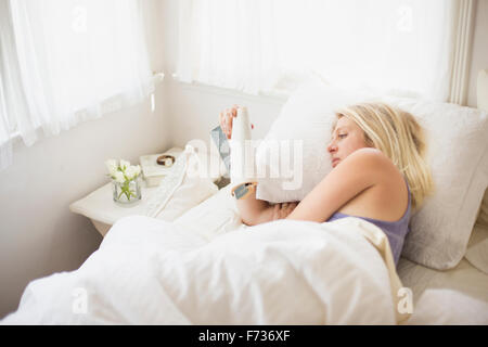 Blonde Frau in einem Bett mit weißem Leinen zu lesen. Stockfoto