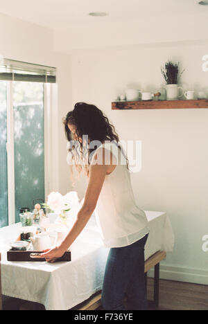 Frau, die ein Tablett mit einer Teekanne und eine Vase mit weißen Rosen auf einem Tisch platzieren. Stockfoto