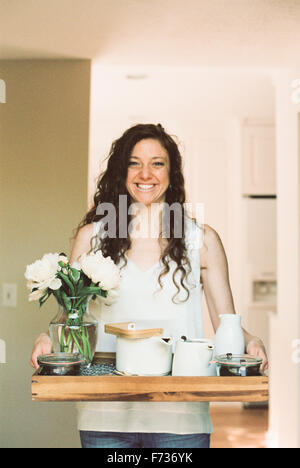 Frau mit einem Tablett mit einer Teekanne und eine Vase mit weißen Rosen. Stockfoto