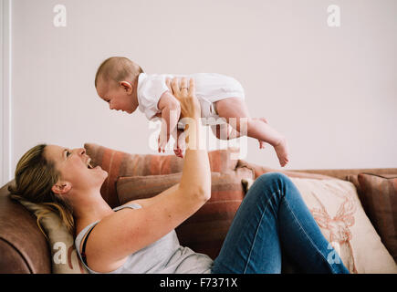 Eine Frau liegt auf dem Sofa mit einem Babymädchen spielen. Stockfoto