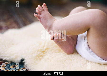 Ein Baby liegend auf einem Schaffell-Teppich, ihre Beine zu treten. Stockfoto