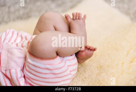 Ein Baby liegend auf einem Schaffell-Teppich, ihre Beine zu treten. Stockfoto