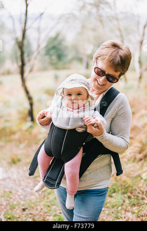 Eine Frau mit Sonnenbrille ein Baby tragen eine weiße Sonnenhut im vorderen Babytragetuch tragen. Stockfoto