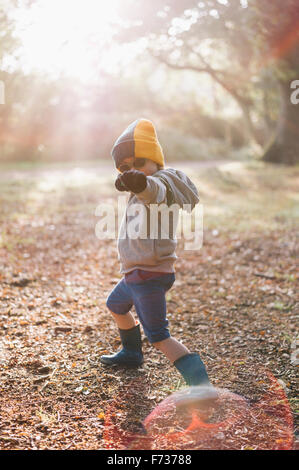 Ein Junge im Freien in eine Wollmütze tragen kurze Hosen und Gummistiefel, auffällig eine Pose mit ausgestrecktem Arm. Stockfoto