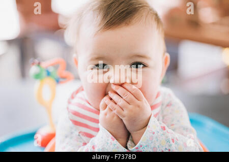 Ein kleines Mädchen mit ihren Händen über den Mund in die Kamera schaut. Stockfoto