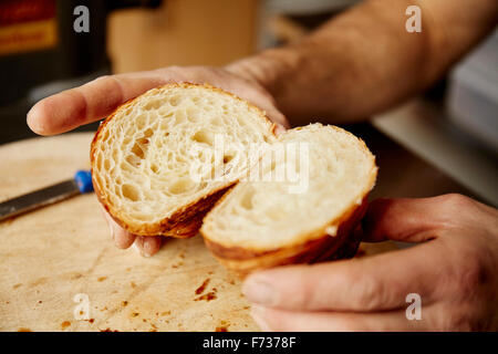 Ein Mann hält eine Croissant in zwei Hälften geschnitten, geschichtet Textur aus gekochtem Teig, das Licht zu zeigen. Stockfoto