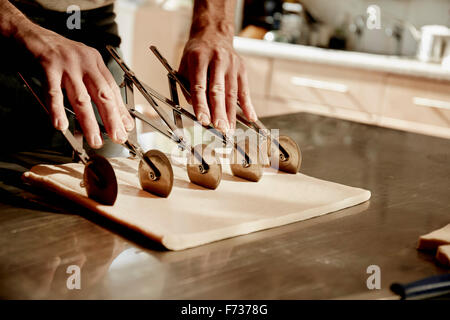 Ein Bäcker arbeiten auf einer bemehlten Fläche teilt den vorbereiteten Teig in Quadrate mit einer erweiterbaren rotary Teig Cutter. Stockfoto