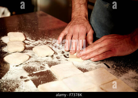 Ein Bäcker arbeiten auf einer bemehlten Arbeitsfläche den vorbereiteten Teig in Quadrate aufzuteilen. Stockfoto