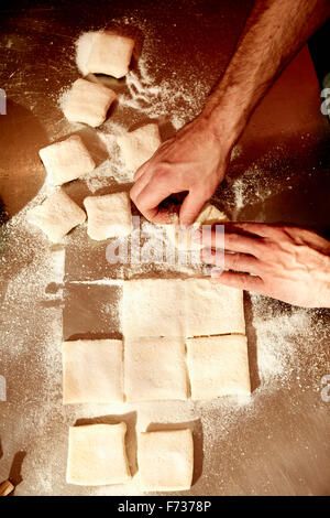 Ein Bäcker arbeiten auf einer bemehlten Arbeitsfläche den vorbereiteten Teig in Quadrate aufzuteilen. Stockfoto