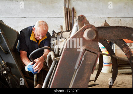 Ein Mann arbeiten mit Werkzeugen auf Bauernhof-Maschinerie in einer Scheune. Stockfoto