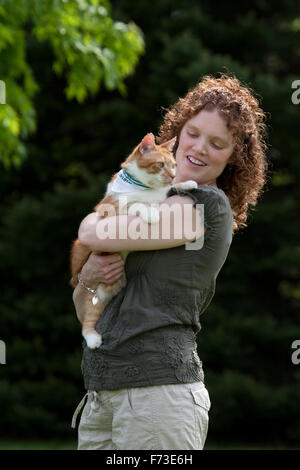 Junge Frau mit roten Haaren hält orange-weiße Tabby Katze Stockfoto