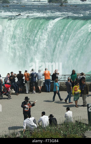 Touristen, die Anzeige der kanadischen Wasserfälle. Horseshoe Falls. Blick von Niagara Falls, Ontario, kan. Mann Gitarre spielen im Vordergrund Stockfoto