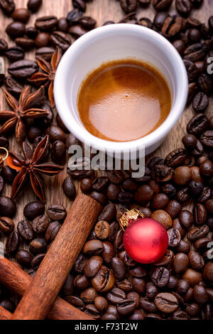 Tasse Kaffee mit Kaffeebohnen, Zimt, Sternanis und rote Weihnachtskugel auf Holz Stockfoto