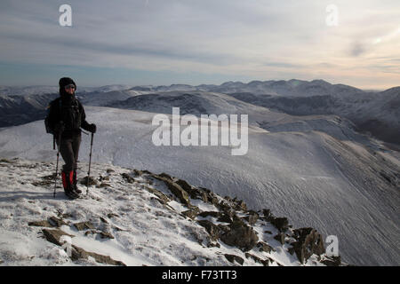 Eine weibliche Wanderer stellt hoch auf einem Berg, im englischen Lake District, im Winter, mit einem Blick zurück über den Weg. Stockfoto