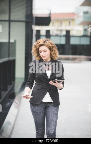 Knie-Figur des jungen schönen kaukasischen zeitgenössische Geschäftsfrau zu Fuß durch die Stadt mit Smartphone und Tablet-Bildschirm-Technologie, Netzwerk, Business, Finanzierungskonzepten suchen Stockfoto