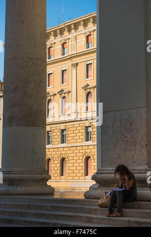 Frau allein am Telefon, Blick auf eine Frau im Schatten, die am Telefon auf den Stufen der Kirche St. Antonius Taumaturgo in Triest, Italien, spricht. Stockfoto