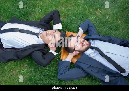 Zwei glückliche junge Geschäftsleute im Anzug auf dem grünen Rasen liegen Stockfoto