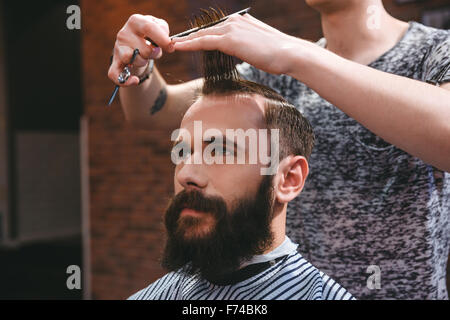 Porträt von schönen jungen Mann mit Bart, einen Haarschnitt mit Kamm und Schere im Friseursalon
