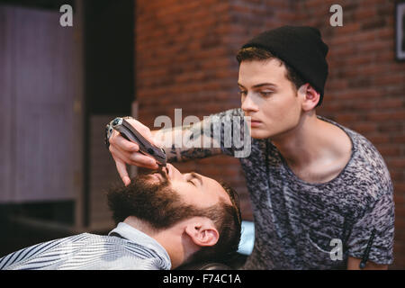 Konzentrierte sich talentierte junge Friseur trimmen Bart hübscher junger Mann im barbershop Stockfoto